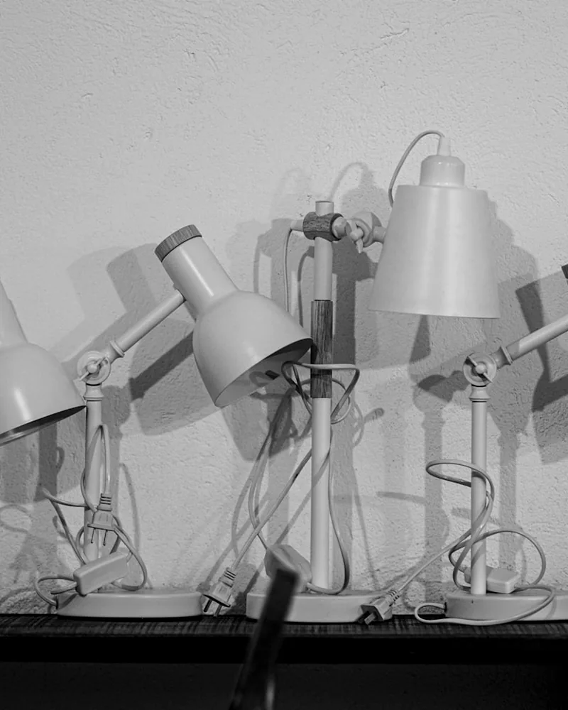 A rhythmic row of silver desk lamps photographed in monochrome