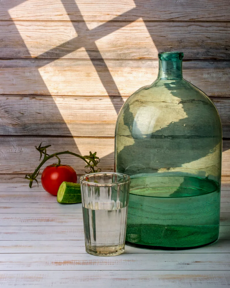 Large green glass carafe with a drinking glass in patterned sunlight