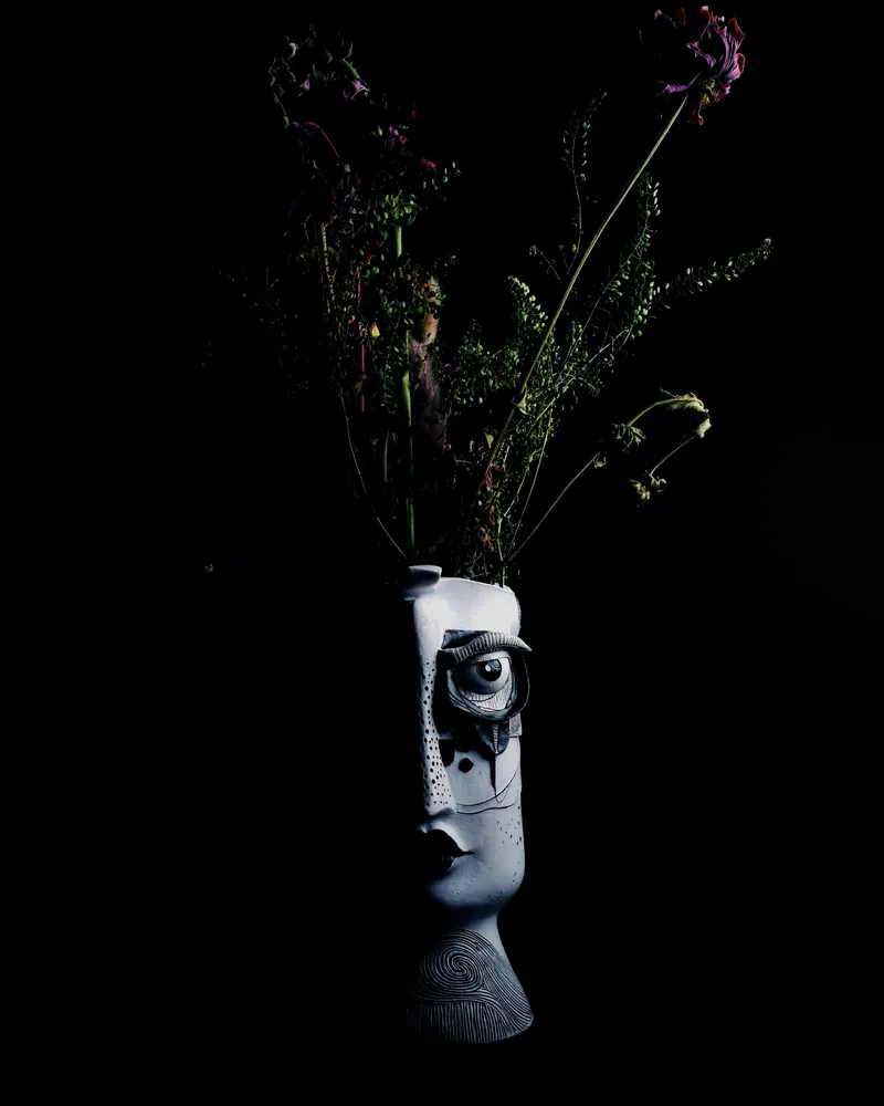 Dark sculptural ceramic object with dried stems against black