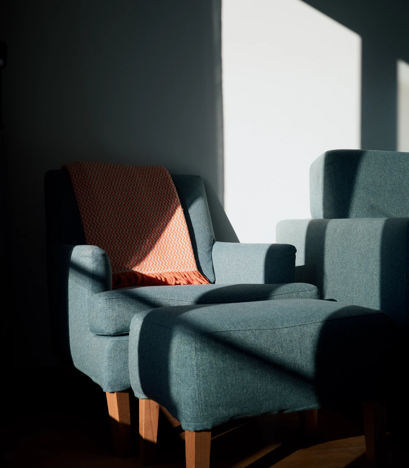 Coral woven throw draped over a blue armchair in sharp afternoon light